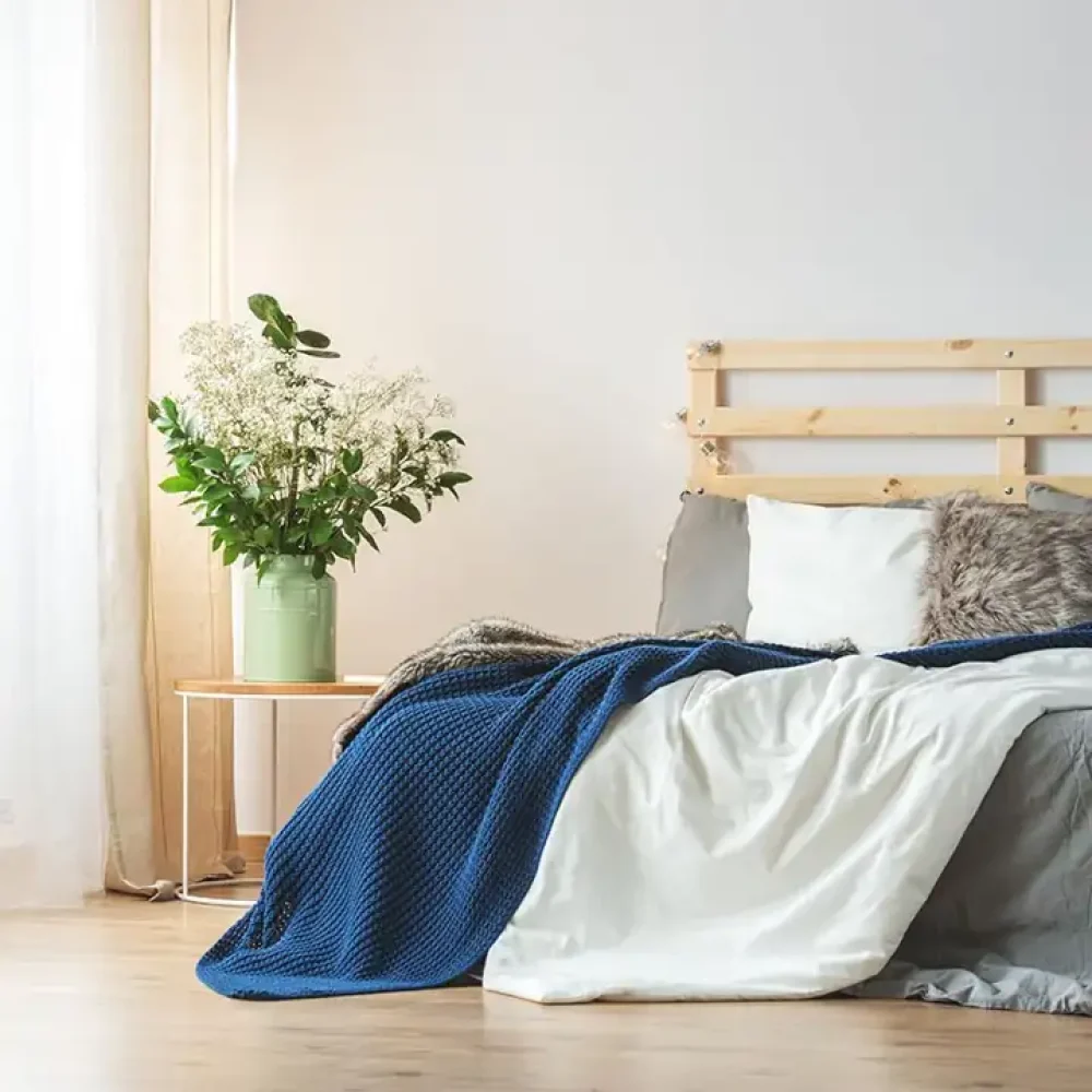 Dormitorio minimalista con cama de madera y manta azul — Mejores Colchones 2026.